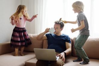 
		Father sitting on couch with two children jumping
	